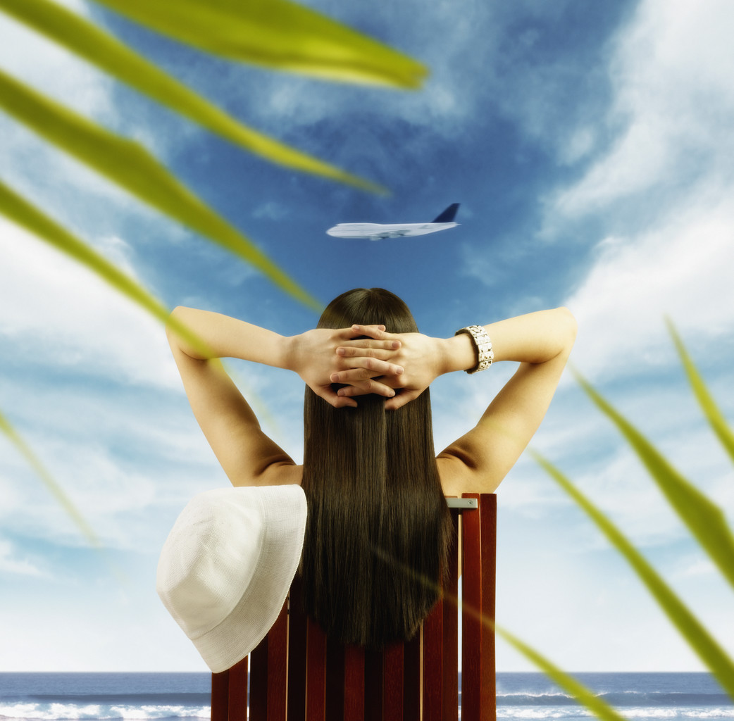 Young woman watching airplane fly by from tropical beach
